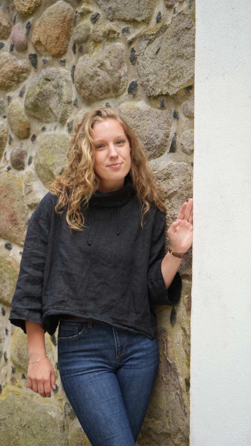 Frau in schwarzer Bluse vor einer strukturierten Steinwand