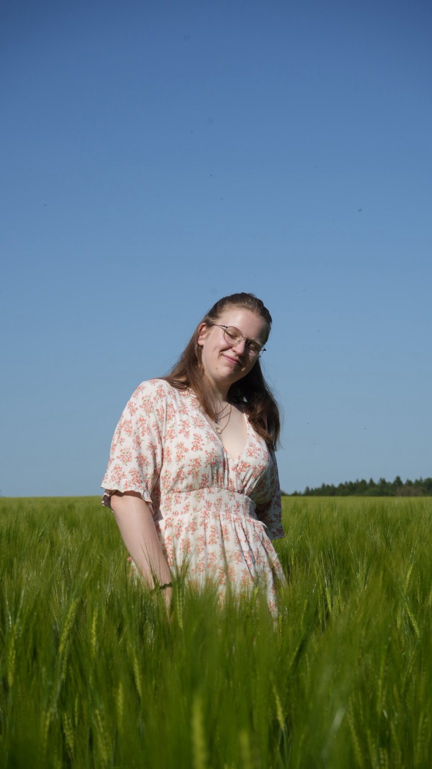 Frau im Blumenkleid in einem grünen Getreidefeld unter blauem Himmel